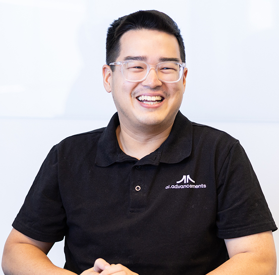 Broadly smiling AI Advancements consultant with glasses in a black AI Advancements polo shirt sitting relaxed with hands together, representing AI Reporting Agents services