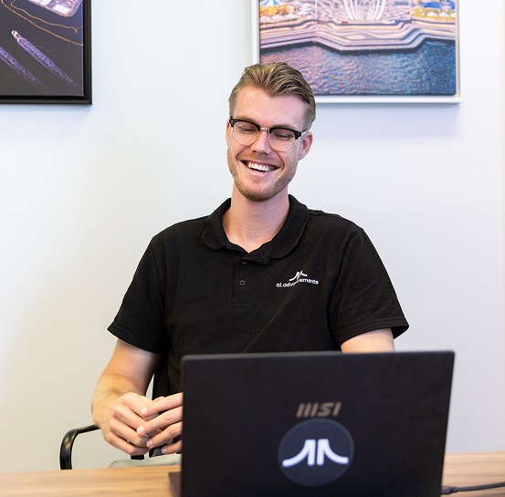 Smiling AI Advancements trainer with glasses and light hair in black polo shirt sitting at an MSI laptop, representing ChatGPT Workshop training services