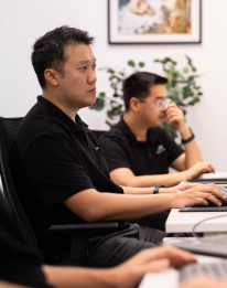 Two professionals in dark shirts collaborating at a computer, representing the AI automation step to automate report creation and insights
