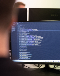 Person working at a large monitor displaying code or terminal, representing the AI strategy step to collect and prioritise AI use cases