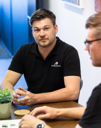 Two professionals in a collaborative discussion around a table, representing the AI chatbot step to design conversation flows that complete work