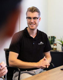 Friendly AI consultant with glasses in dark shirt seated at a table, representing the first step of free consultation and problem definition