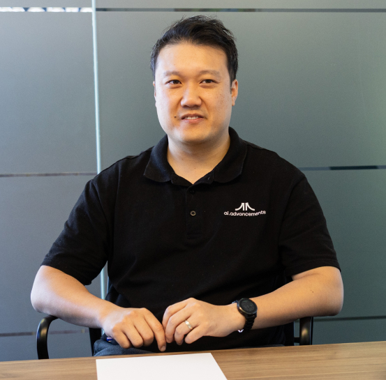 AI Advancements professional in black polo shirt sitting at a desk with hands folded in a modern office, representing AI for Leaders executive training services