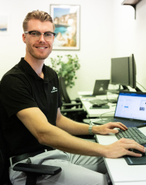 Smiling professional with glasses in dark shirt working at a computer setup, representing the AI strategy step to move into delivery
