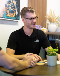 AI chatbot consultant with glasses in dark shirt seated with hands clasped, representing the AI chatbot step to refine, expand and scale case uses