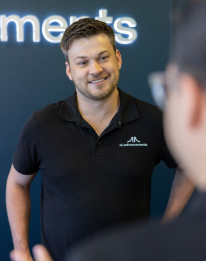 AI Advancements consultant presenting and smiling in front of branded backdrop, illustrating the step to understand your reporting process and bottlenecks