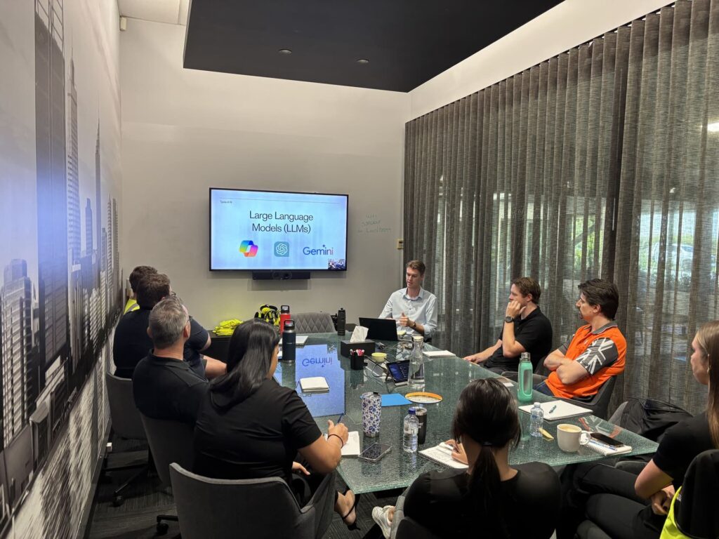 Business leaders and professionals in a boardroom attending AI Leadership Training with a presentation screen showing Large Language Models including Microsoft Copilot, OpenAI and Google Gemini logos