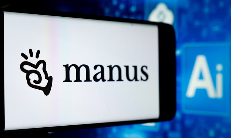 Manus AI logo displayed on a smartphone screen with AI keyboard key visible on blue technology background
